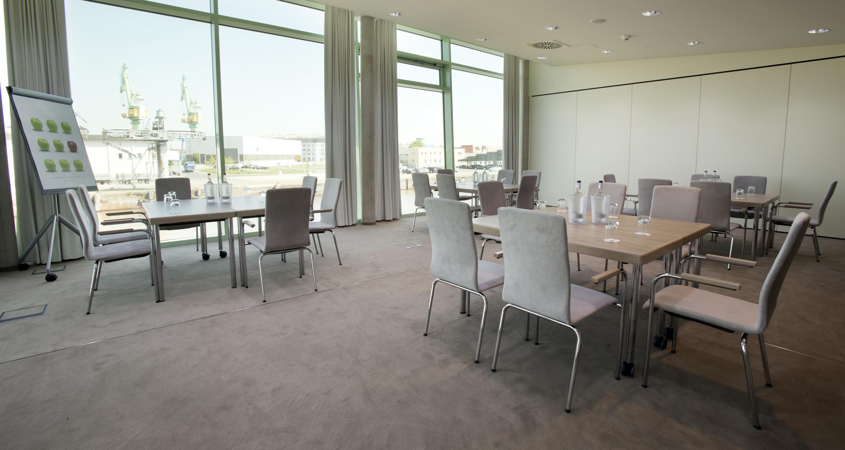 Un salón de conferencias con mesas y sillas, ventanas amplias y vistas al exterior.