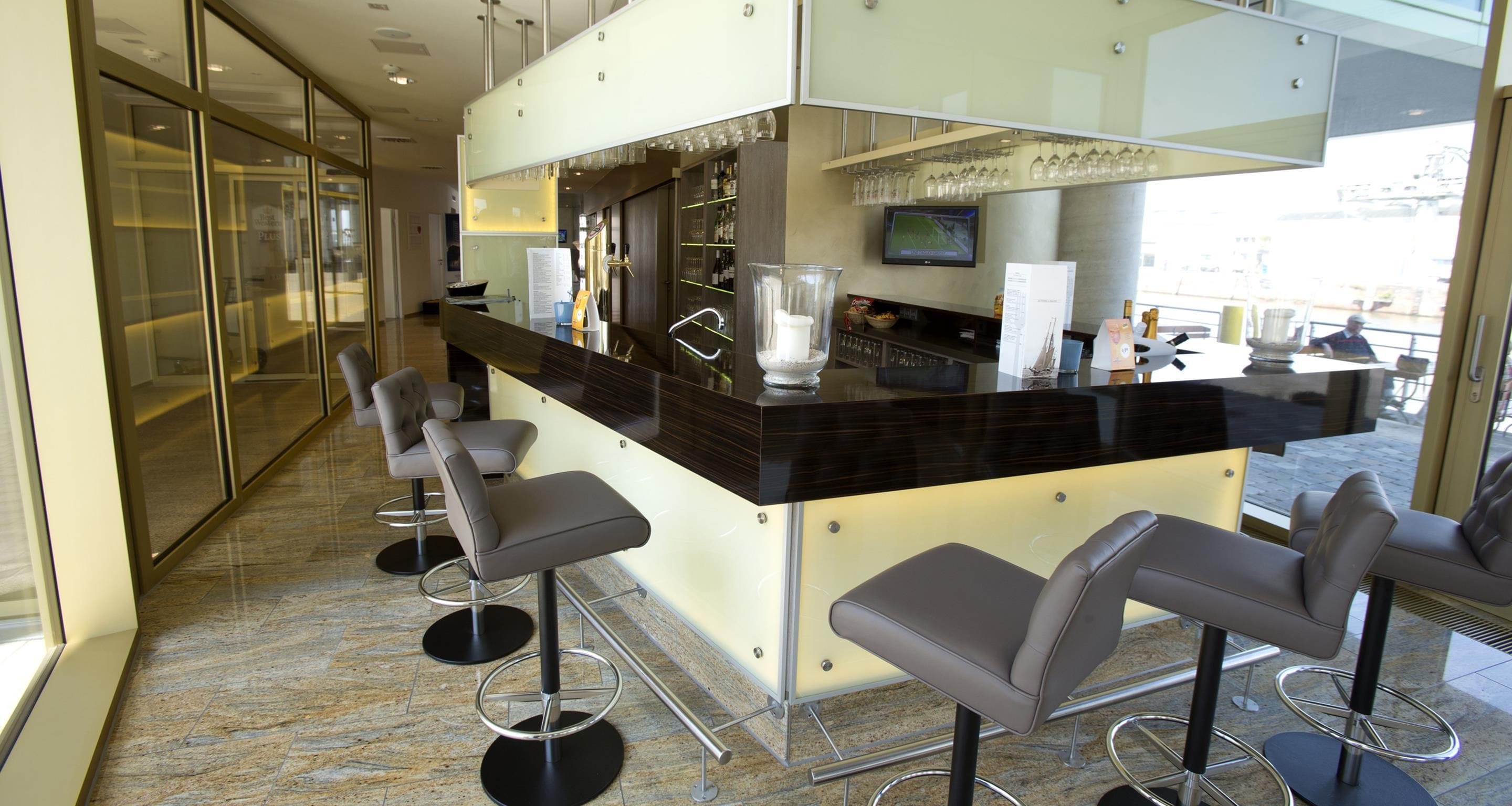 Een moderne bar met een marmeren vloer, barstoelen, een balie met een televisie en uitzicht op de stad.