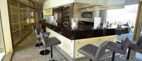 Un espace bar moderne avec un sol en marbre, des tabourets de bar, un comptoir doté d’un téléviseur et une vue sur la ville.
