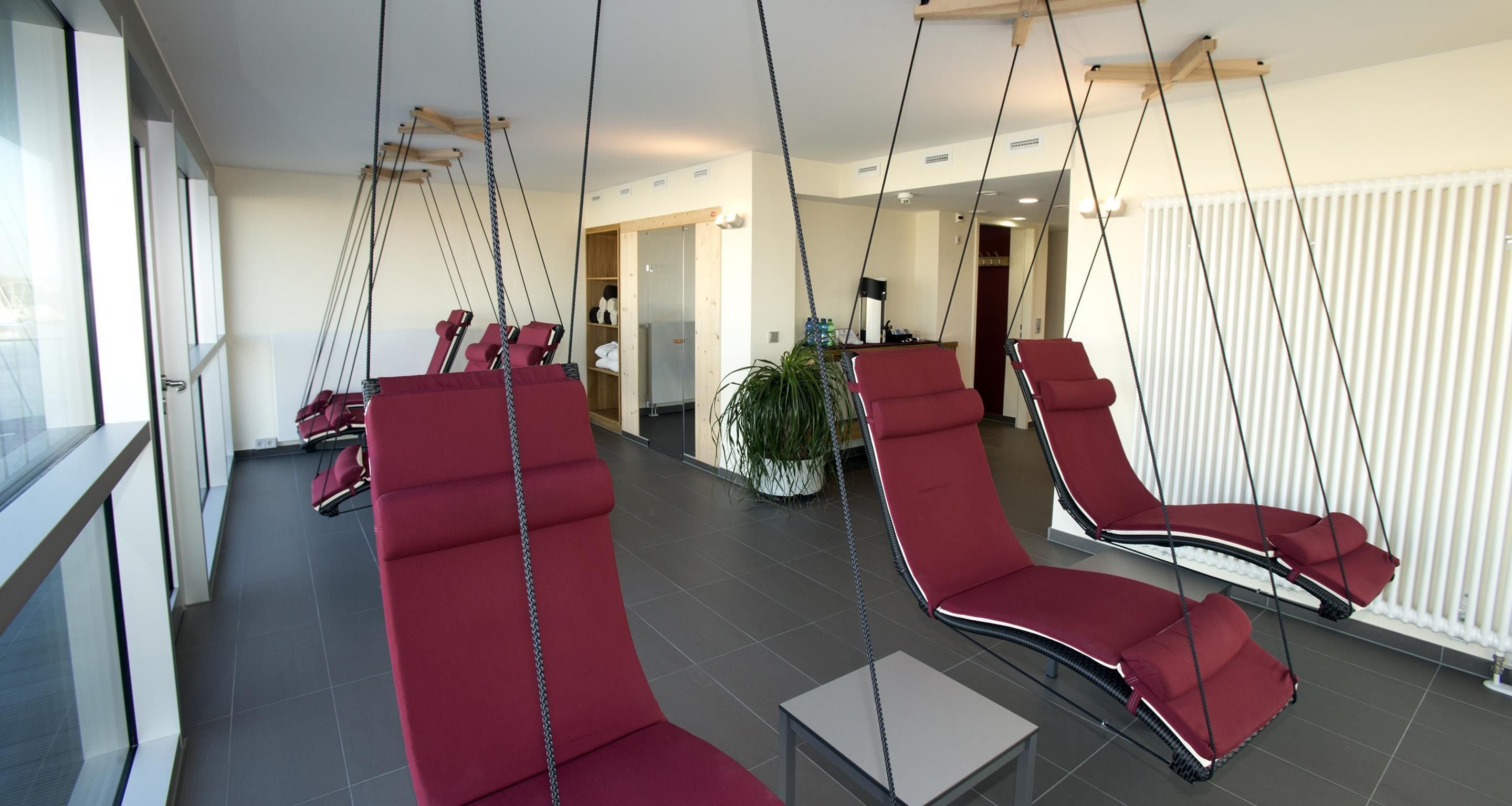 Un interior moderno con sillones rojos suspendidos del techo, una planta en maceta y vista a un pasillo.