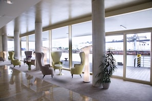 A spacious lobby with modern chairs, large windows, and a view of a water body and industrial structures. - Best Western Plus Hotel Bremerhaven (Bremerhaven)