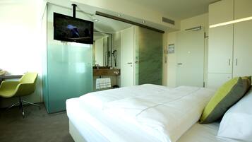 A hotel room with a bed, a TV, a desk with a chair, and a bathroom with a mirror and towel rack.
