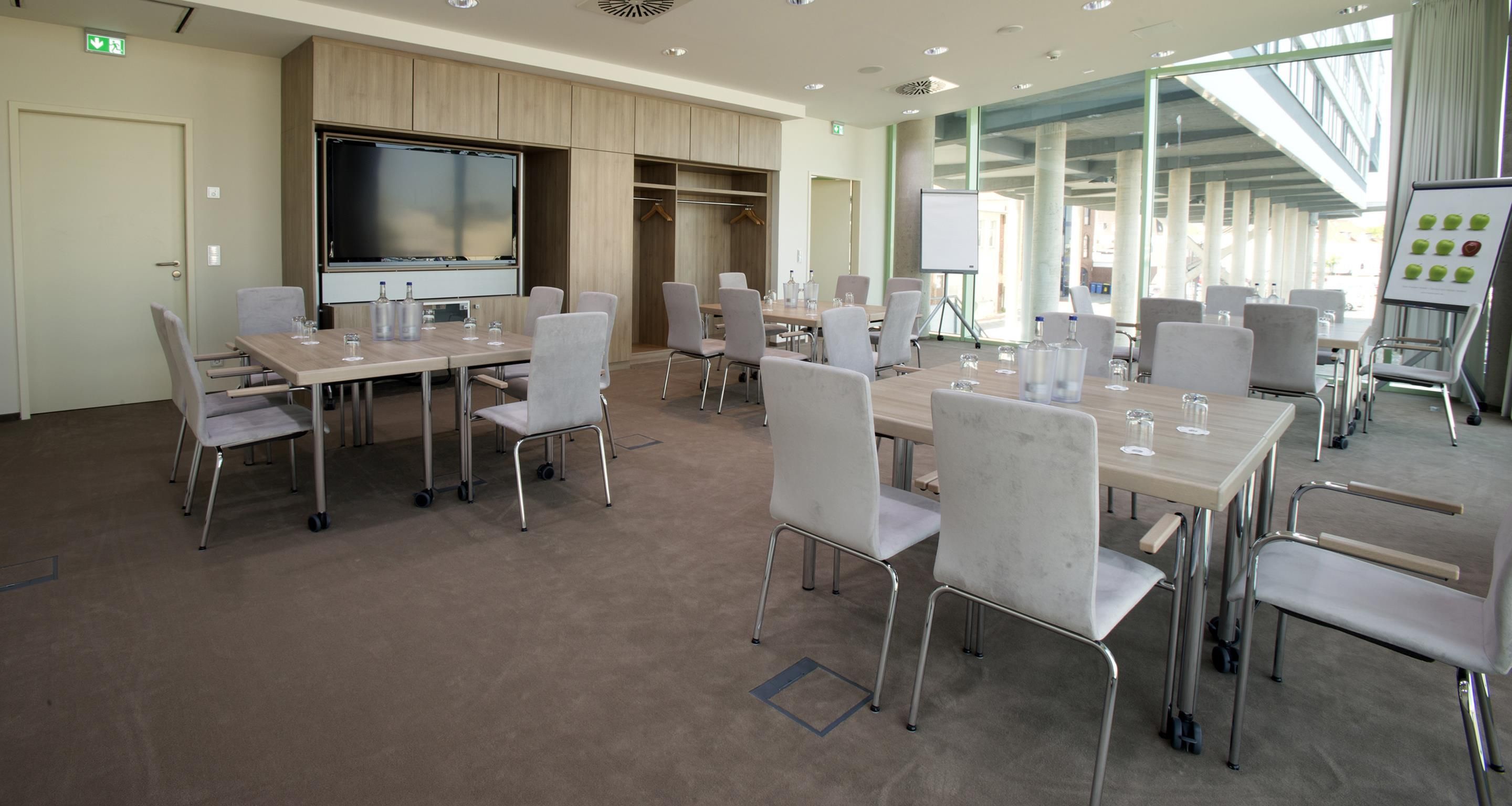 A conference room with tables, chairs, a large screen, and a whiteboard.