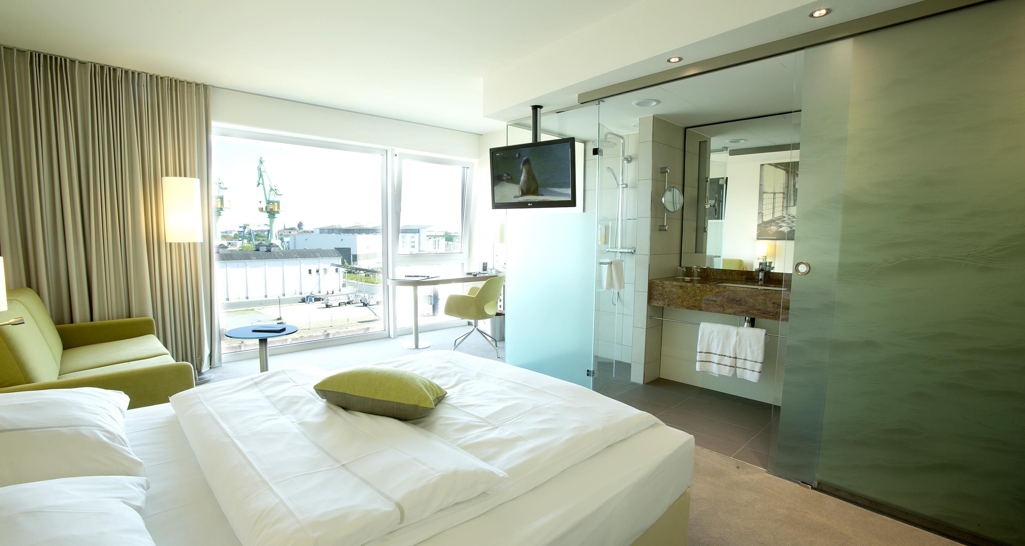 A hotel room with a bed, a desk, a chair, a television, and a bathroom with a mirror and sink.