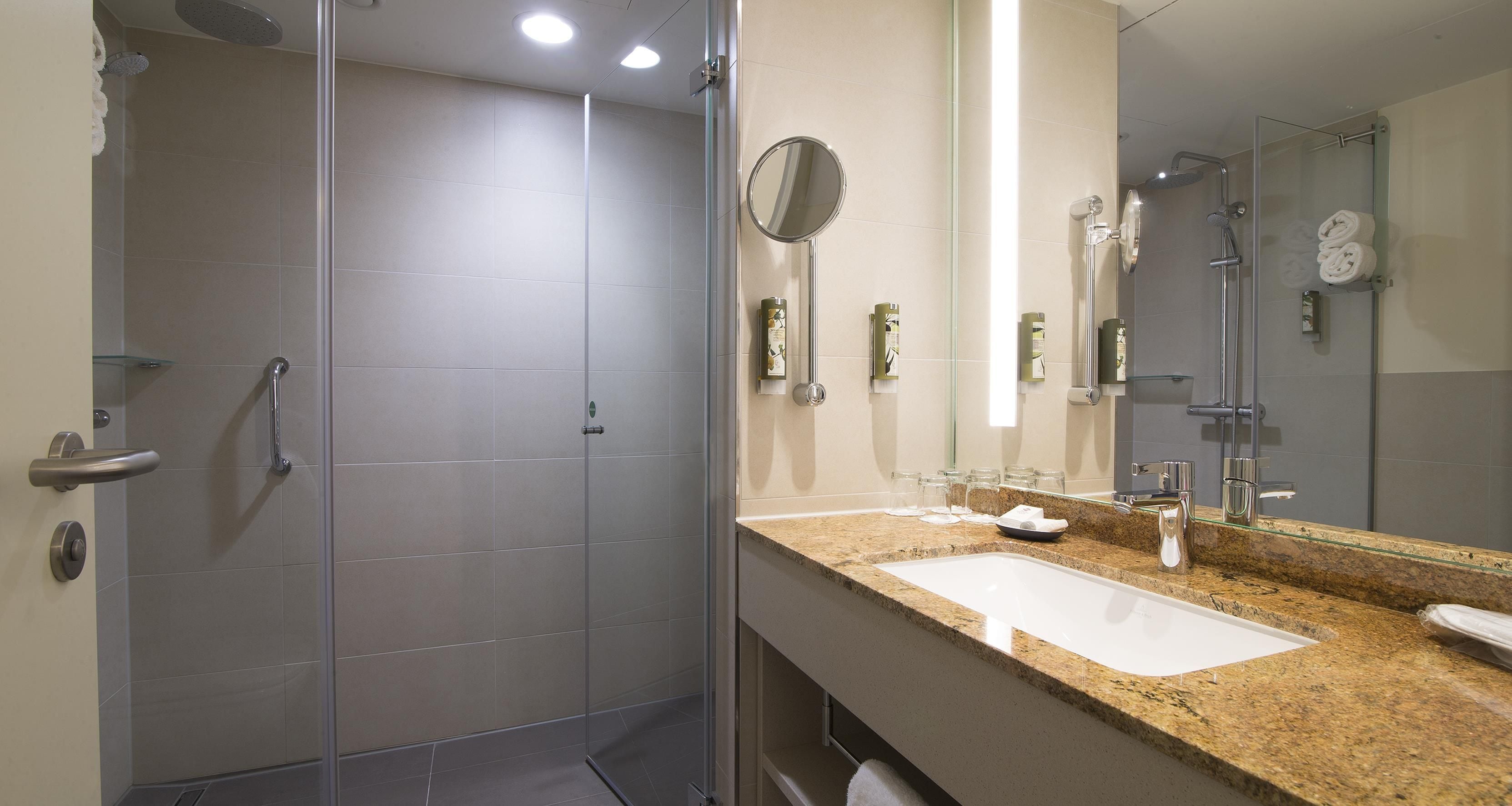 A modern bathroom with a glass shower enclosure, a sink with a granite countertop, and a large mirror.