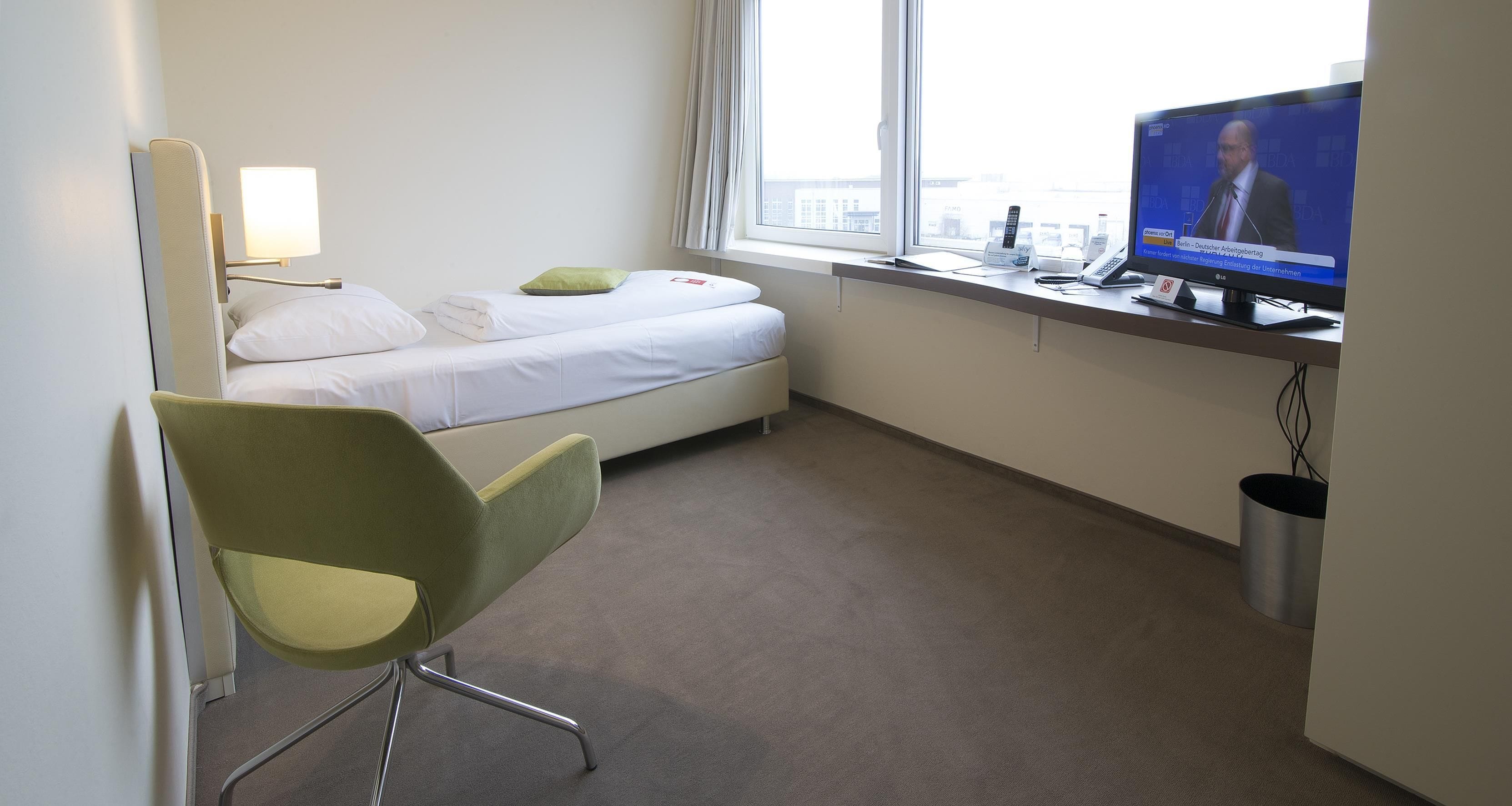 Habitación de hotel con una cama, un escritorio con televisor, una silla y una ventana.