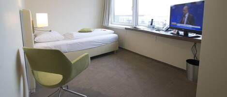 A hotel room with a bed, a desk with a television, a chair, and a window.