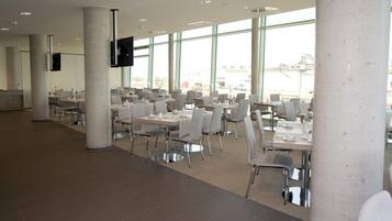 A spacious indoor dining area with multiple tables and chairs, large windows, and a modern architectural design.