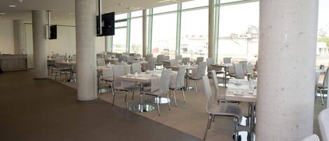 A spacious indoor dining area with multiple tables and chairs, large windows, and a modern architectural design.