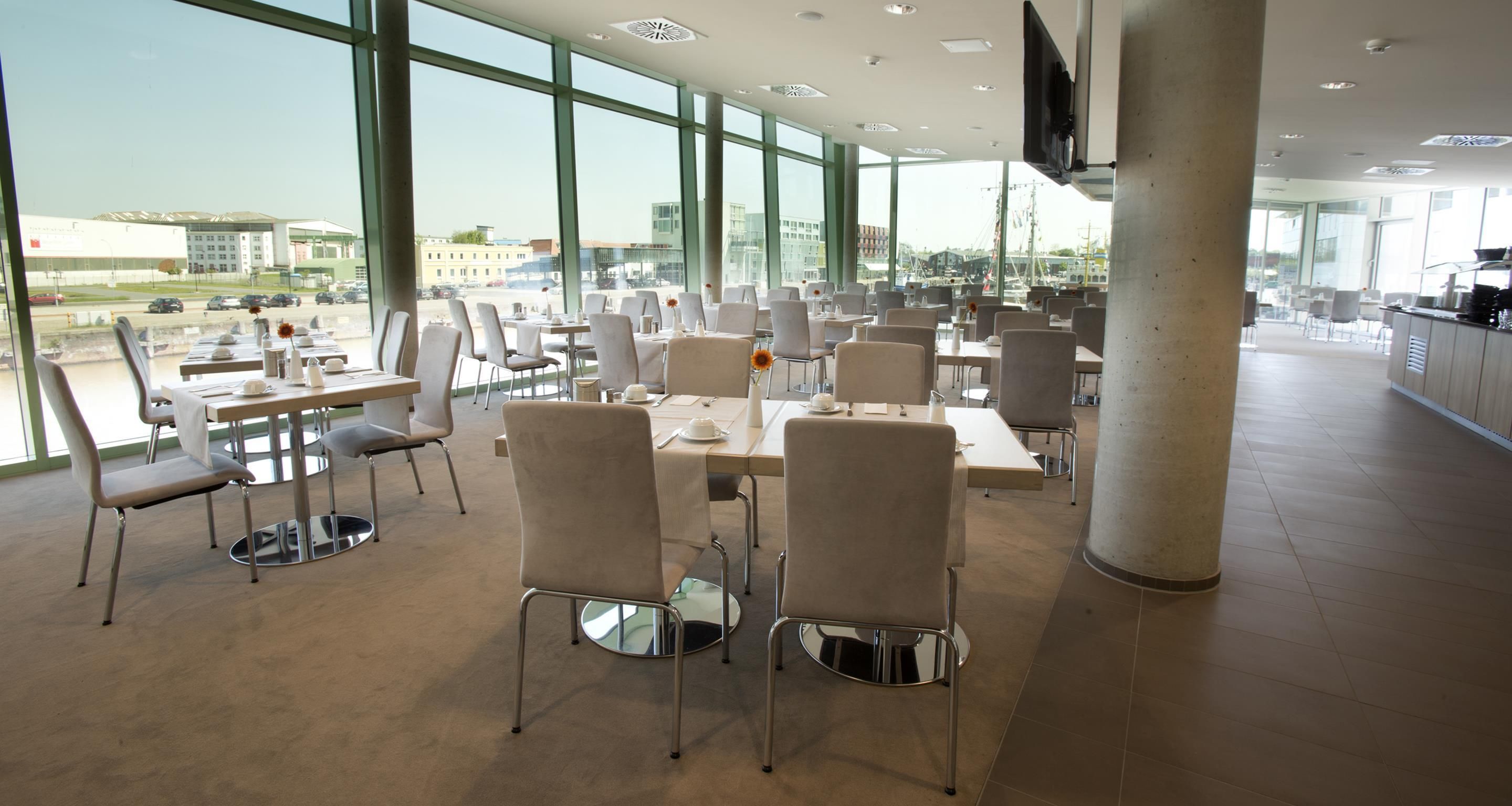 A spacious indoor dining area with multiple tables and chairs, large windows offering a view of the outside, and a modern architectural design.