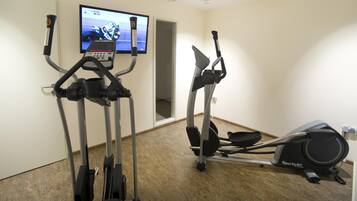 A fitness room with two elliptical machines and a television displaying a racing event.