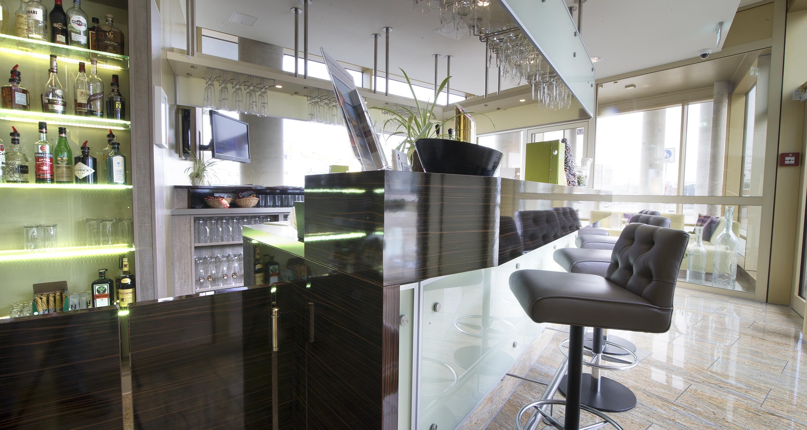 Una zona de bar moderna con separador de vidrio, taburetes y una variedad de botellas de licor.