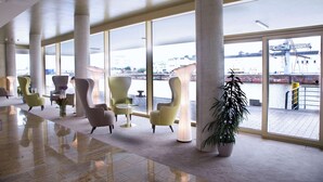A spacious lobby with large windows, modern chairs, and a potted plant. - Best Western Plus Hotel Bremerhaven (Bremerhaven)