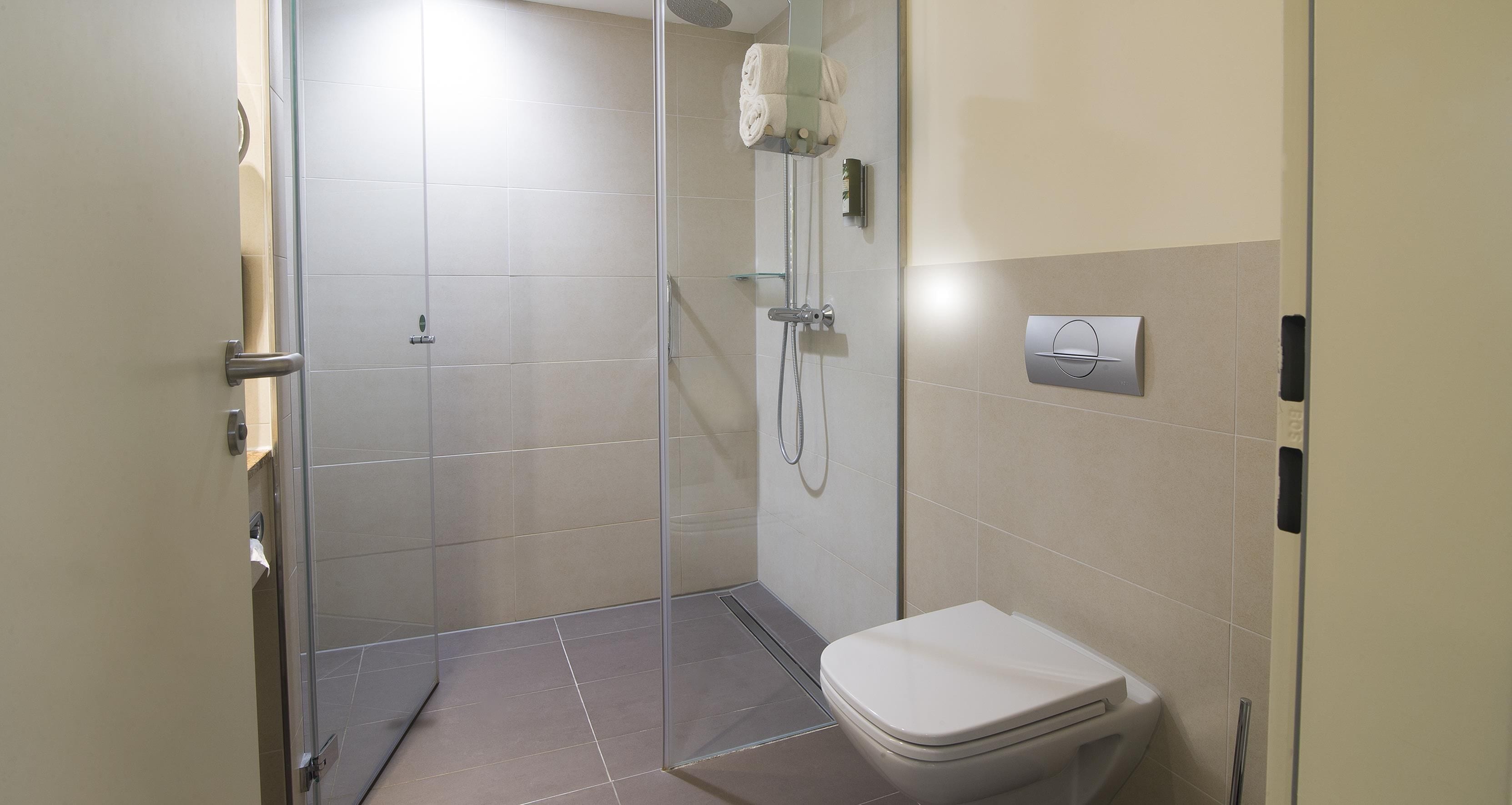 A modern bathroom with a glass-enclosed shower, a toilet, and a wall-mounted faucet.