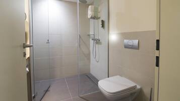 A modern bathroom with a glass-enclosed shower, a toilet, and a wall-mounted faucet.