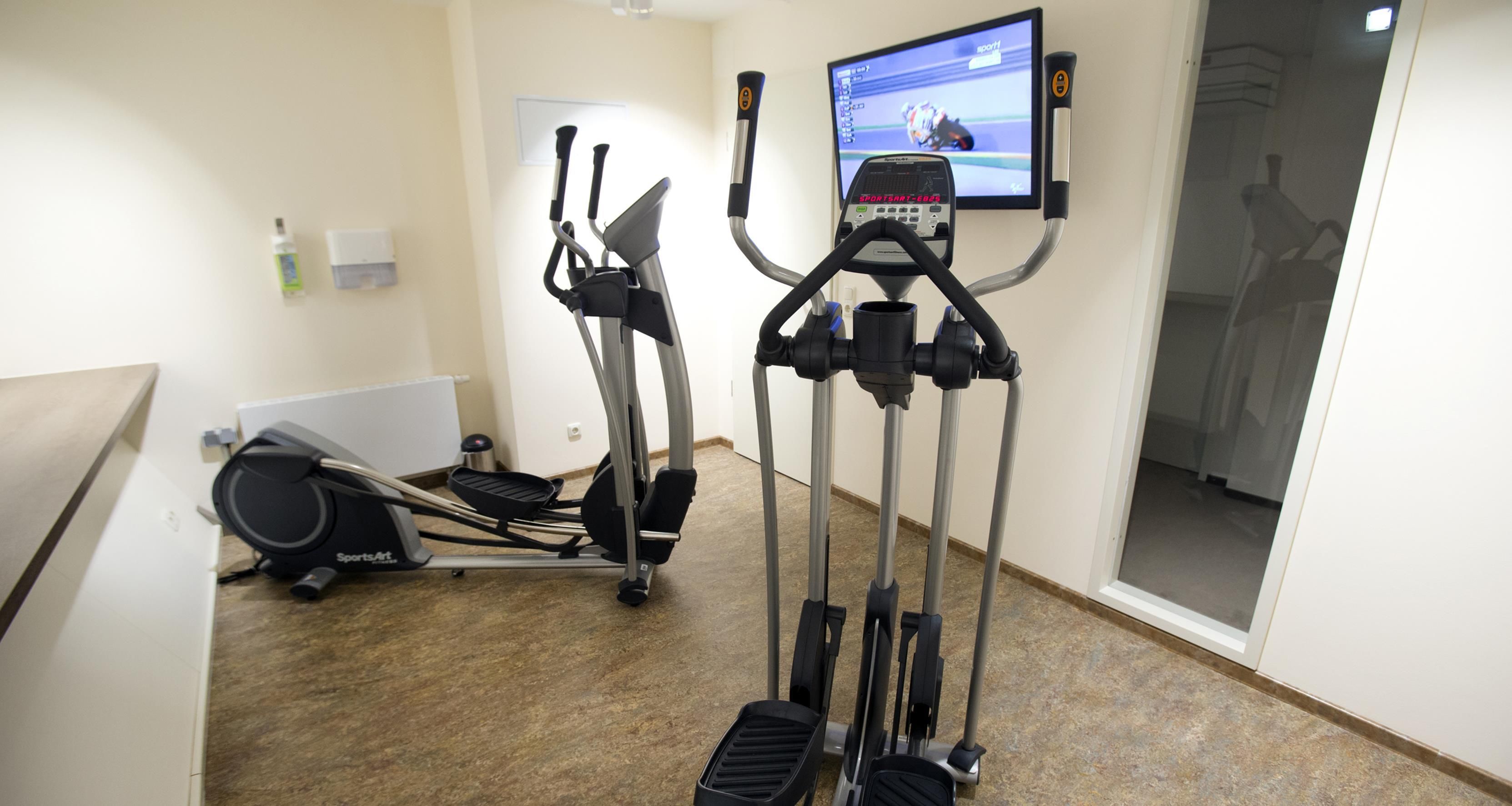 A gym with stationary bikes, an elliptical, and a television displaying a sports channel.