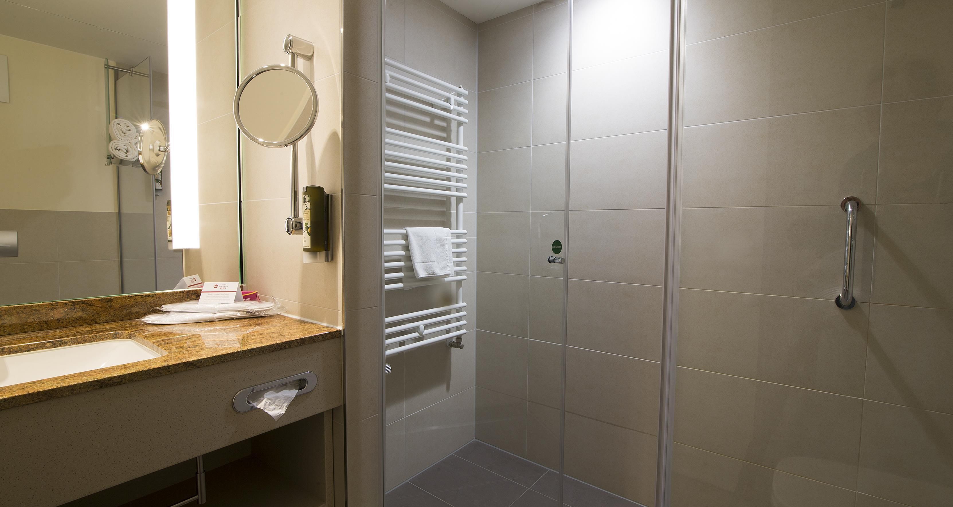Un bagno moderno con un piano di marmo, uno specchio rotondo, un porta asciugamani e una cabina doccia in vetro.
