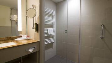 Un bagno moderno con un piano di marmo, uno specchio rotondo, un porta asciugamani e una cabina doccia in vetro.