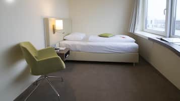 Een hotelkamer met een eenpersoonsbed, een stoel, een nachtkastje, een lamp en een raam met uitzicht op gebouwen.