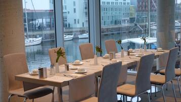 A dining area with a view of a canal and boats, featuring a long table set for four with chairs, vases with flowers, and a menu on the table.