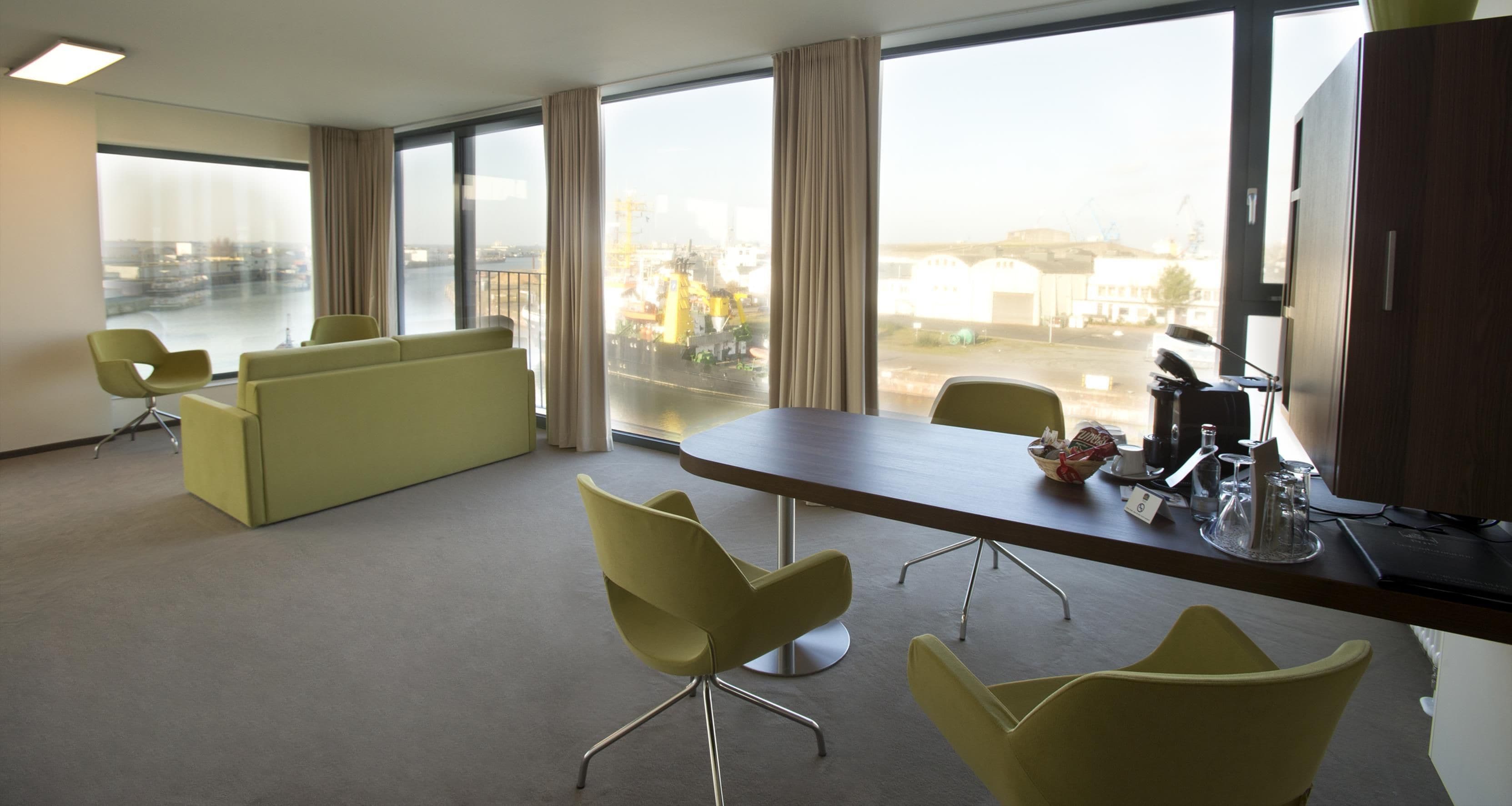 A modern office space with a large window, a conference table, and yellow chairs.