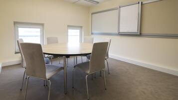 A conference room with a round table, four chairs, two windows, and a whiteboard on the wall.