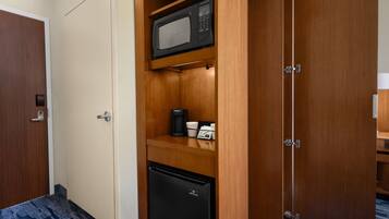 Habitación compacta con microondas, cafetera y refrigerador pequeño.
