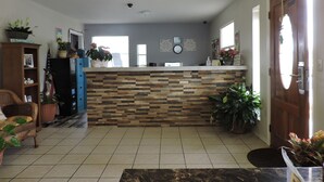 A spacious living room with a tiled floor, a wooden reception desk, and various potted plants. - Riata Inn Crystal City (Crystal City)