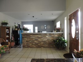 Un amplio salón con suelo de baldosas, un mostrador de recepción de madera y diversas plantas en macetas.
