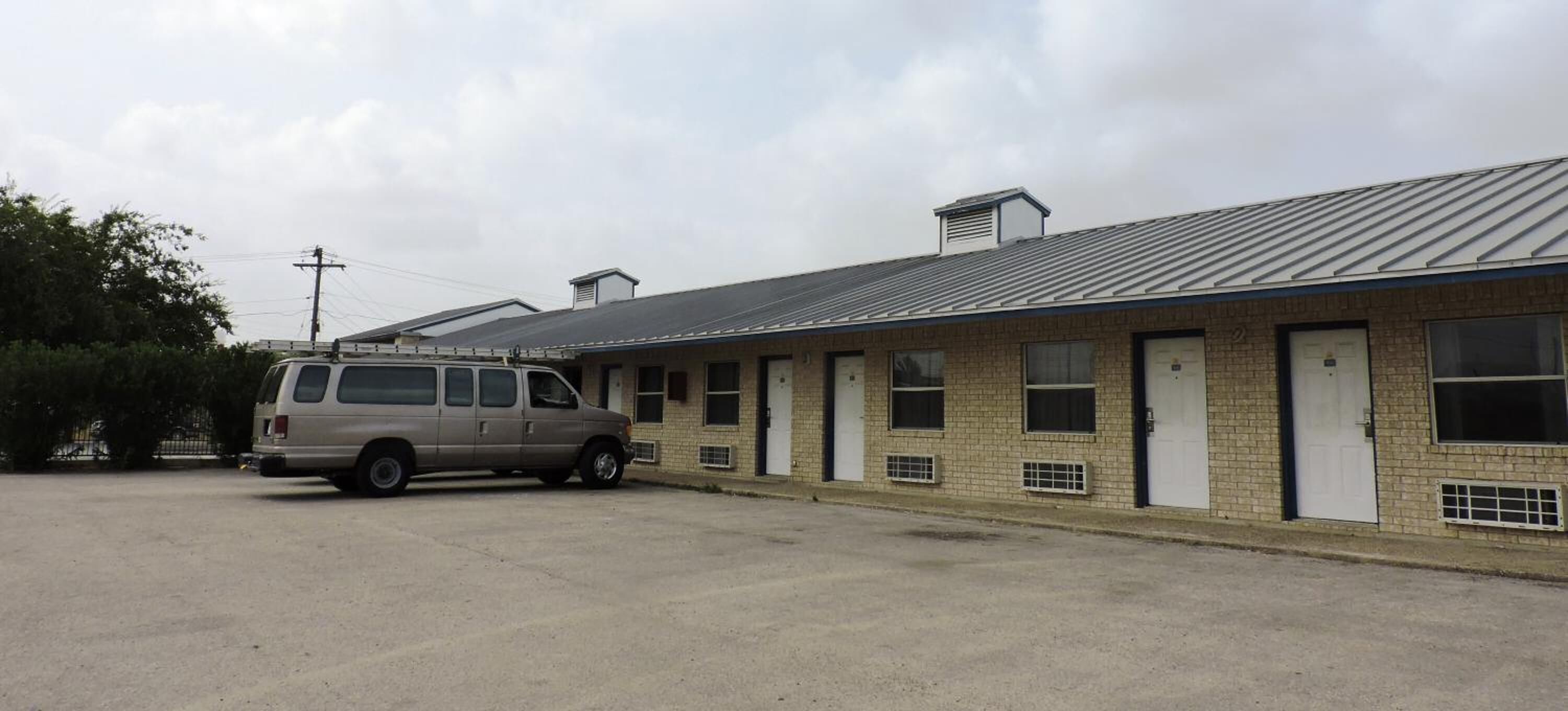 Un motel d’un seul étage, avec une rangée de chambres, chacune dotée d’une porte et d’une fenêtre. Un fourgon est garé dans l’allée.