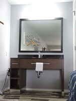 Un baño con un espejo grande, toallero, lavamanos y un armario.