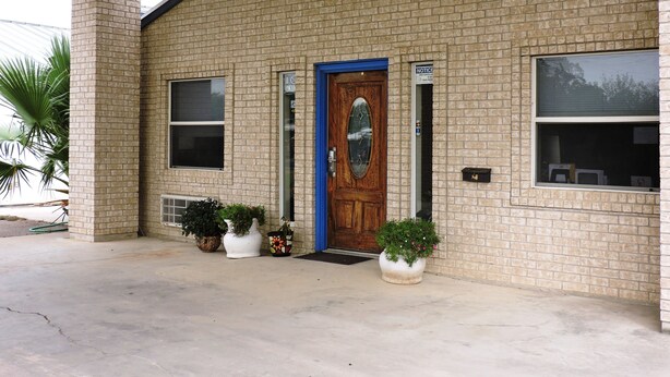 A two-story brick building with a front door, windows, and potted plants. - Riata Inn Crystal City (Crystal City)