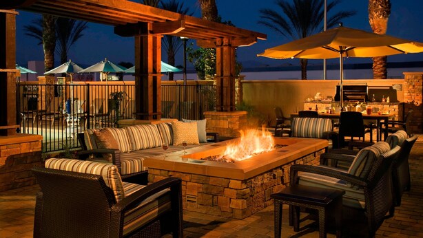 An outdoor patio with a stone fire table, wicker furniture, and umbrellas. - Residence Inn Tustin Orange County (Tustin)