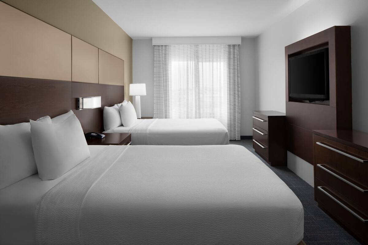 A hotel room with two beds, a TV, a desk, and a window with curtains.