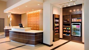 A hotel reception area with a modern design, a reception desk, a wall with a geometric pattern, and a refrigerated display case with beverages. - Residence Inn Tustin Orange County (Tustin)