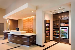 A hotel reception area with a modern design, a reception desk, a wall with a geometric pattern, and a refrigerated display case with beverages. - Residence Inn Tustin Orange County (Tustin)