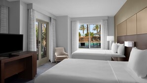 A hotel room with a large bed, a desk with a TV, a chair, and a window with a view of palm trees and a pool. - Residence Inn Tustin Orange County (Tustin)