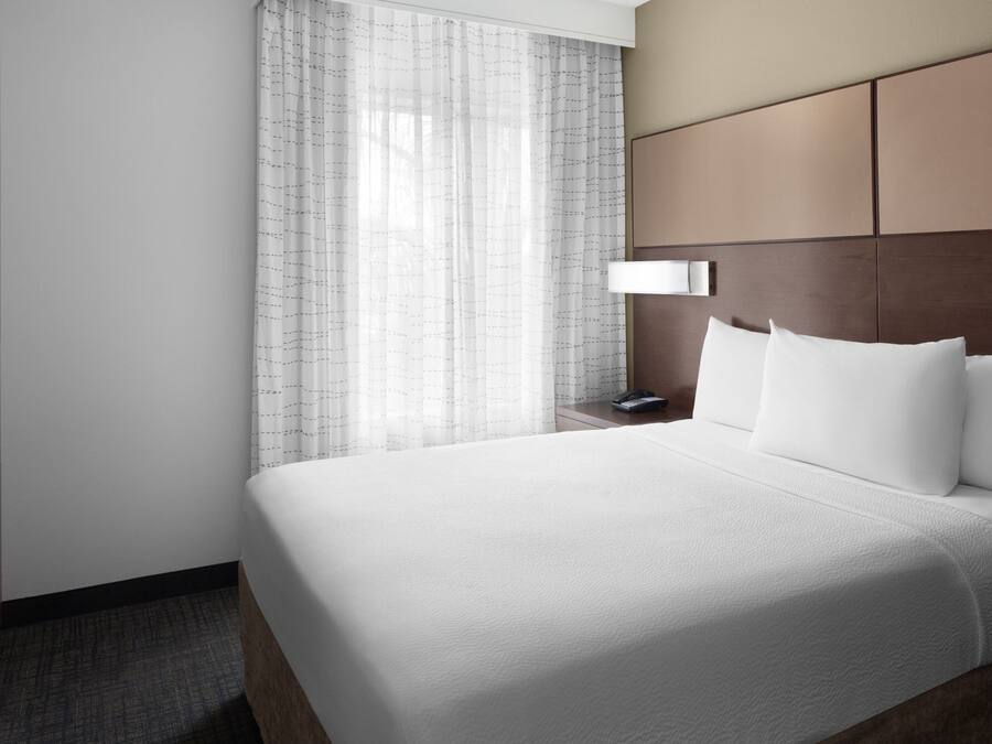 Une chambre d’hôtel avec un grand lit, une table de chevet, une lampe et une fenêtre avec des rideaux.