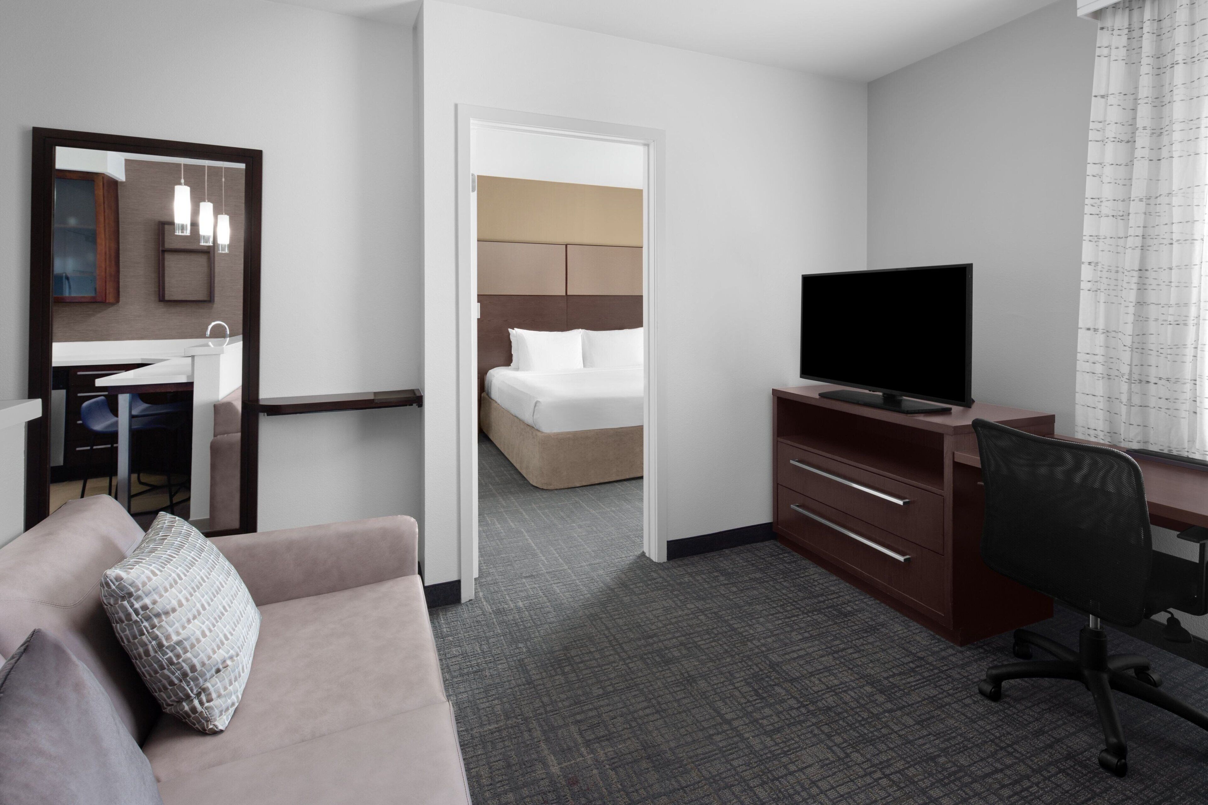 A hotel room with a bed, a desk, a television, a sofa, and a bathroom visible through an open door.