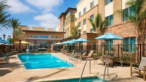 A hotel pool area with lounge chairs and umbrellas, surrounded by a stone wall and palm trees. - Residence Inn Tustin Orange County (Tustin)
