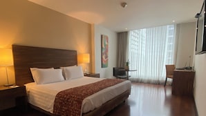 A hotel room with a large bed, two bedside lamps, a desk with a chair, a potted plant, and a window with curtains. - Hotel Estelar Calle 100 (Bogotá)