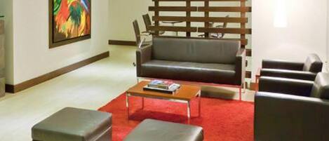 A modern living room with a grey sofa, two ottomans, a coffee table, and a red carpet.