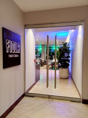 A hotel entrance with a glass door, a potted plant, and a sign reading "FIOLA TRATTORIA". - Hotel Estelar Calle 100 (Bogotá)