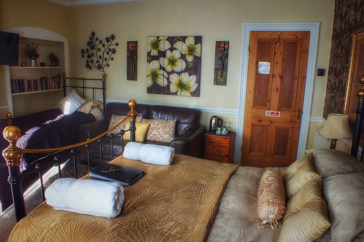 A hotel room with a bed, a sofa, a small table, a bookshelf, and a door with a sign.