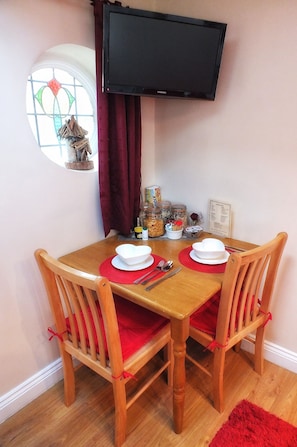 Un comedor con una mesa y sillas de madera, un televisor montado arriba y una ventana con cortinas.