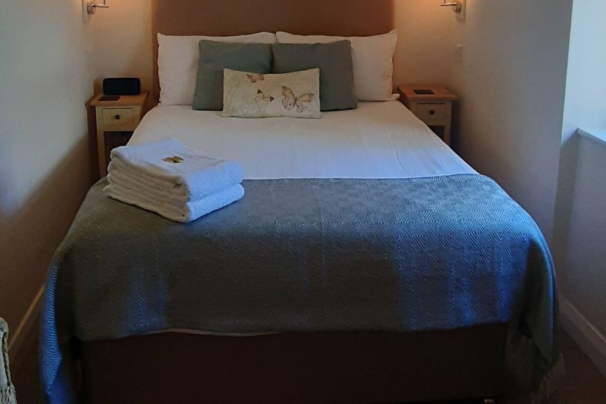 Un lit bien fait, recouvert d’une couverture bleue, avec deux lampes de chevet et un élément décoratif accroché au mur au-dessus.