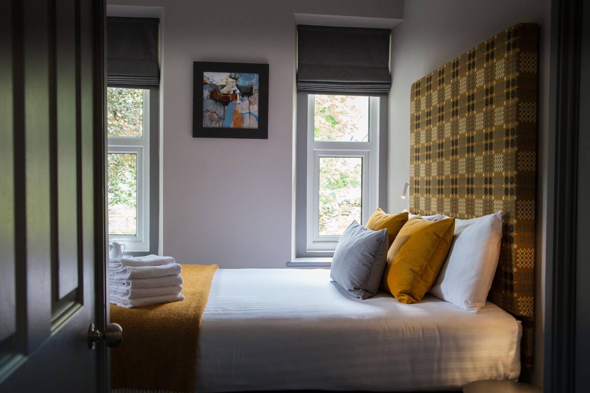 Une chambre à coucher avec un lit, deux fenêtres, un tableau et un mur à motifs.