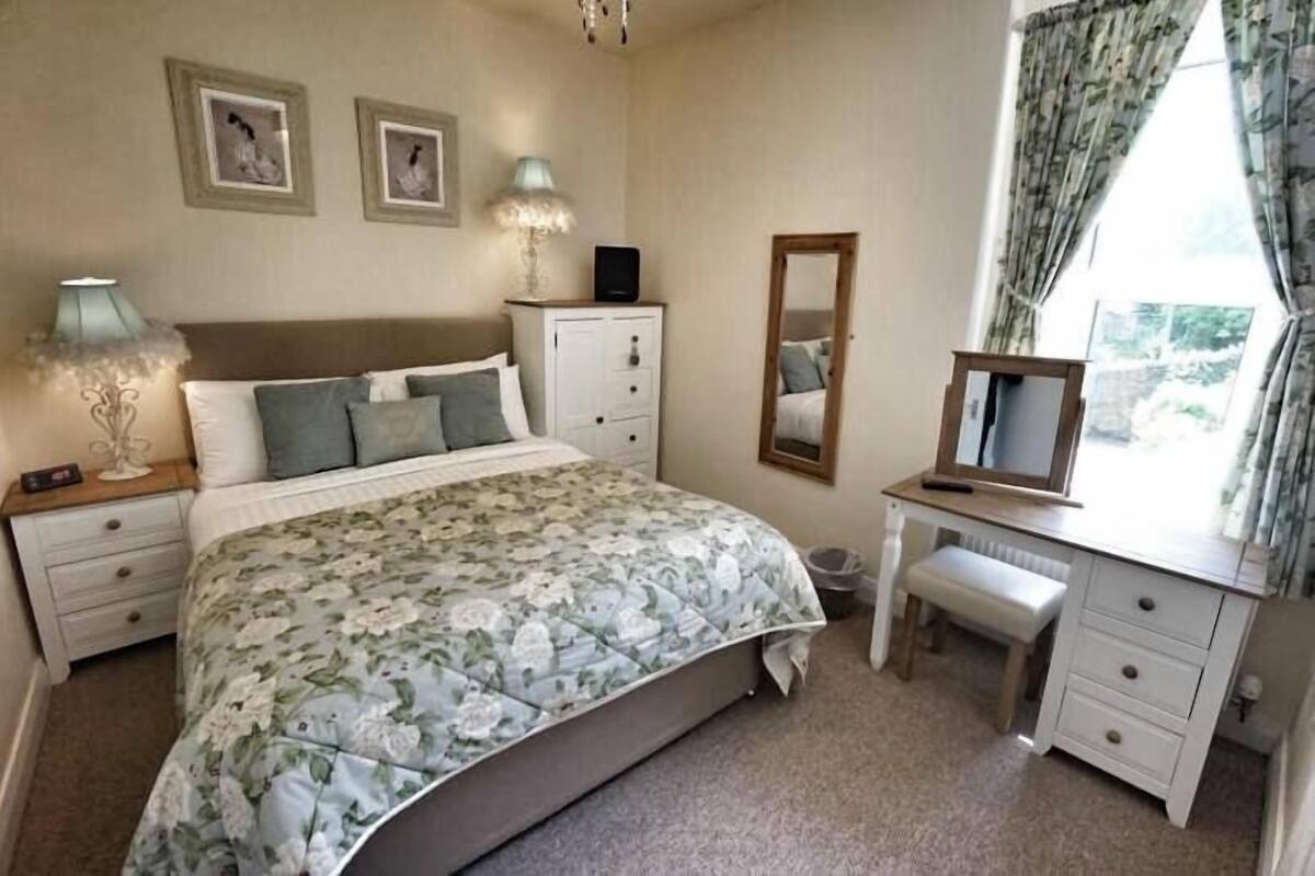 Une chambre à coucher comprenant un lit, des tables de chevet, une commode, un miroir et une fenêtre avec des rideaux.
