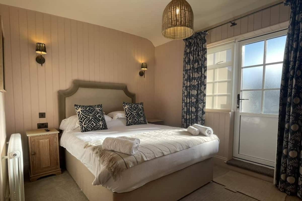 A bedroom with a large bed, two bedside lamps, a radiator, and a window with curtains.