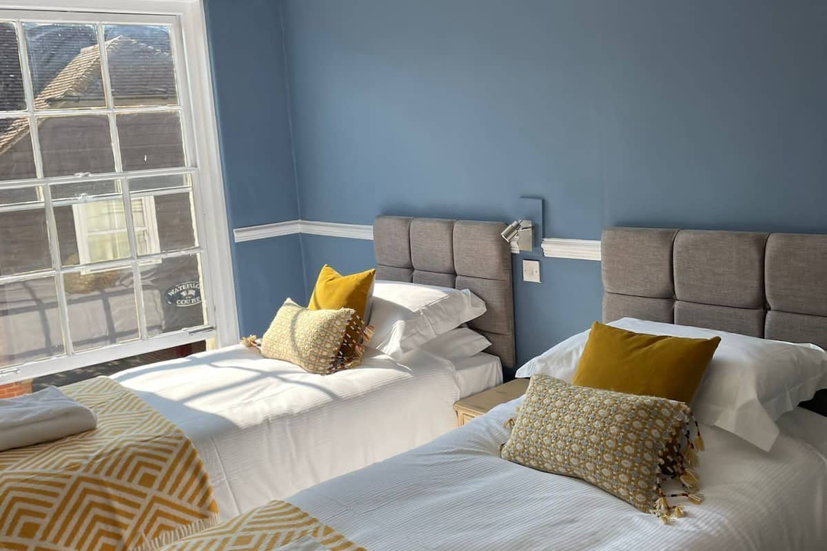 A hotel room with two beds, a large window, and a chandelier.